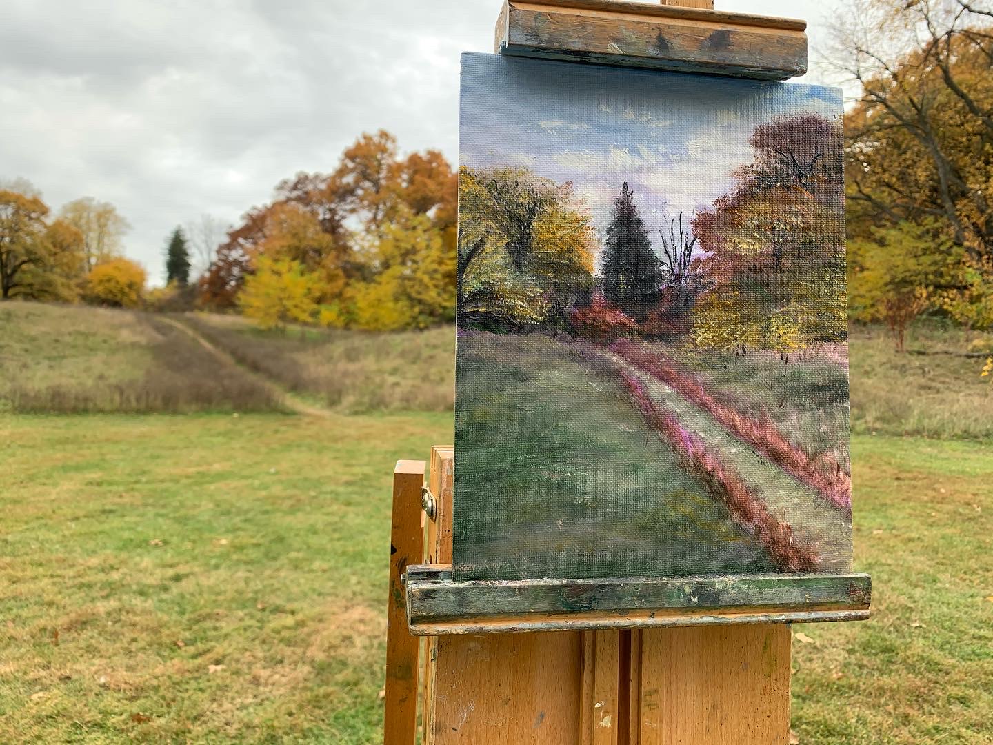 A plein air oil painting on an easel in an autumn field